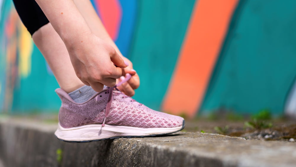 young woman tying her shoelaces outdoors training road